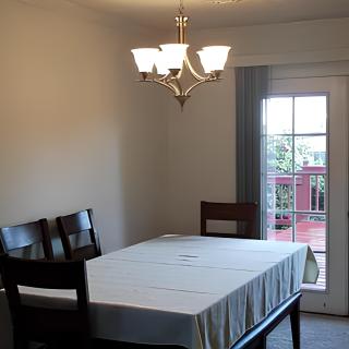 A minimalist dining room with a table, chairs, and a chandelier by the window.