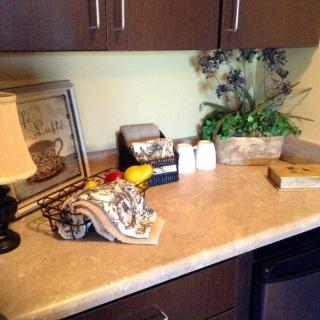 A kitchen counter with decorative items, including a lamp, framed artwork, and a flower arrangement.