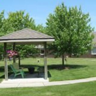 A small gazebo with benches surrounded by a well-maintained lawn and trees.