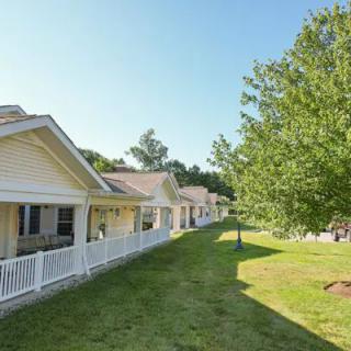 A row of houses with porches under a clear blue sky, surrounded by trees and grassy areas.