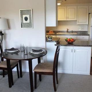 A modern dining area adjacent to a kitchen, featuring a round table set with place settings and a fruit bowl on the counter.