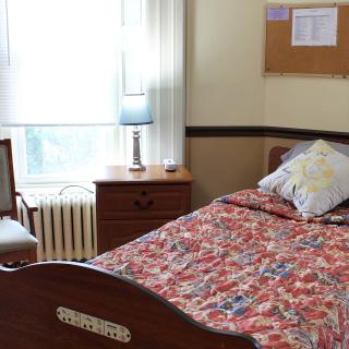 A cozy bedroom with a single bed, nightstand, and lamp near a window.