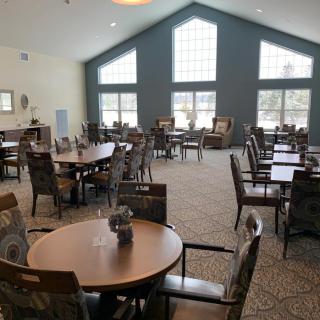 A spacious dining area with multiple tables and chairs, featuring large windows that allow natural light to fill the room.