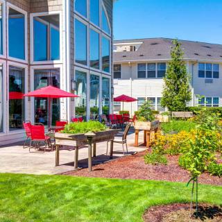A sunny outdoor patio area with red umbrellas and seating, surrounded by a landscaped garden.