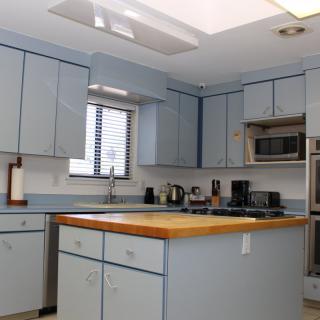A modern kitchen with light blue cabinets, wooden countertop, and various appliances.