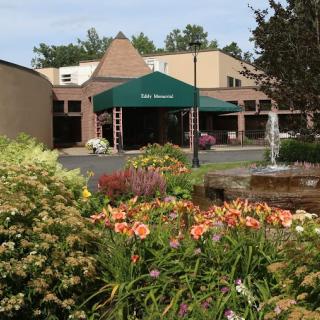 A welcoming entrance to a building surrounded by vibrant flowers and a tranquil fountain.