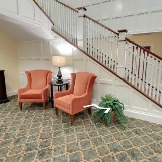 A cozy seating area with two orange armchairs and a lamp near a staircase.