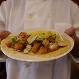 A chef presenting a plate of delicious tacos topped with fresh ingredients.