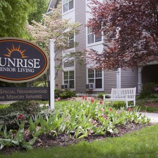 The front entrance of an assisted living facility with well-maintained gardens and a welcoming sign.