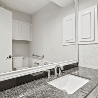 A modern bathroom with a granite countertop and large mirror.