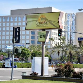 A brightly colored restaurant sign in an urban setting, surrounded by palm trees and modern buildings.
