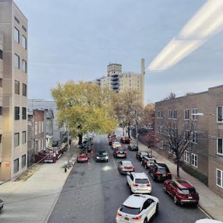 A view of a bustling urban street lined with parked cars and golden autumn trees.