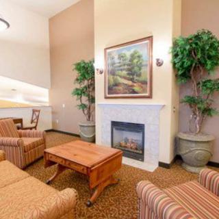 A cozy living room with comfortable seating around a fireplace, adorned with plants and a landscape painting.