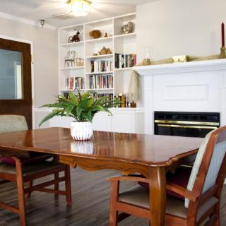 A cozy dining room with a wooden table, chairs, and an indoor plant, complemented by a white fireplace and built-in bookshelf.