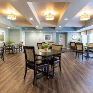 A modern dining room with neatly arranged tables and chairs, featuring elegant lighting and hardwood flooring.