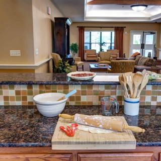 A kitchen countertop with baking utensils and a tomato on a cutting board, overlooking a living room area.