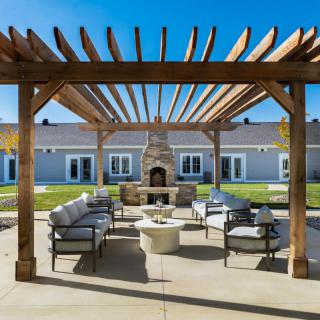 A beautifully designed outdoor patio area with a pergola, comfortable seating, and a central fireplace.