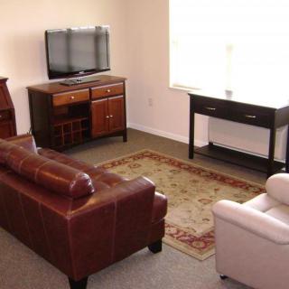 A cozy living room with a leather sofa, armchair, TV, and a patterned rug.