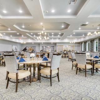 An elegant dining area with neatly arranged tables and chairs, illuminated by chandeliers.
