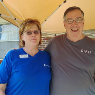 Two individuals pose together under a tent, showcasing a friendly atmosphere.