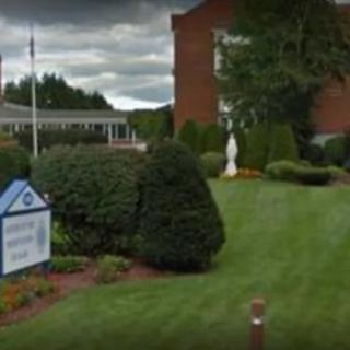 A landscaped area with a sign and statue in front of a brick building on a cloudy day.
