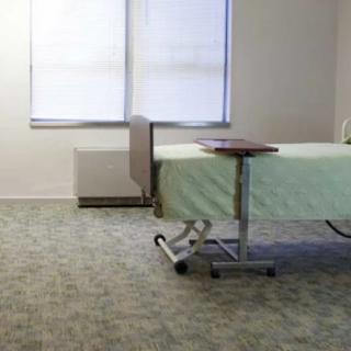 A hospital room with a single bed and an adjustable table by the window.