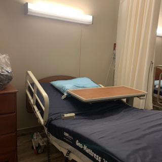 A hospital bed in a patient room, equipped with a bedside table and basic amenities.
