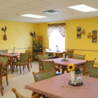 A cozy dining room with multiple tables and chairs, decorated with yellow walls and floral arrangements.