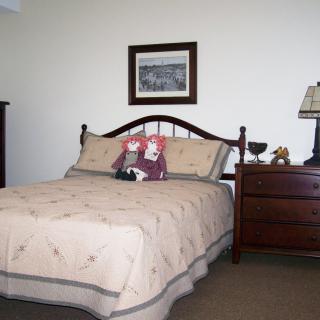 A cozy bedroom featuring a bed with dolls and a nightstand with a lamp.