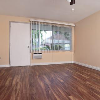 An empty living room with wood flooring and large window blinds.