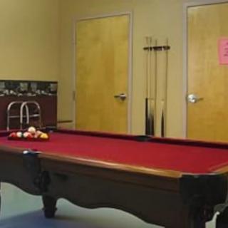 A game room featuring a red pool table with cue sticks on the wall.