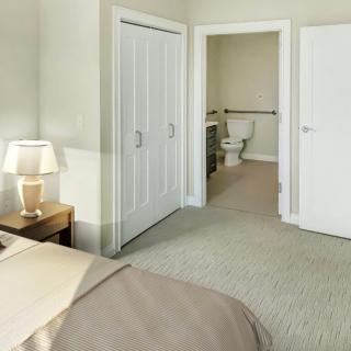 A cozy bedroom with a view into an adjacent bathroom, featuring a bed, lamp, and closet.