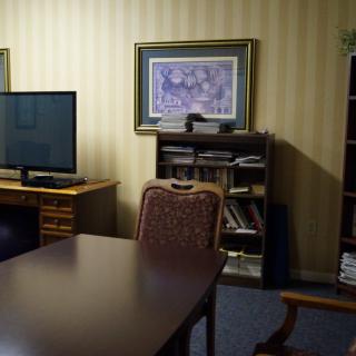 A cozy office setup with a desk, chairs, a TV, and a bookshelf.