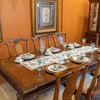 A dining room features a wooden table set elegantly with glassware and decorative ceramic plates, complemented by a patterned table runner.