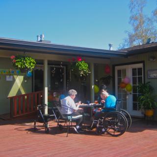 Two people enjoying a conversation at an outdoor patio on a sunny day.