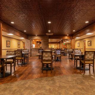 A warmly lit restaurant interior with wooden floors and empty tables.