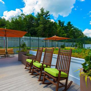 A rooftop garden with wooden rocking chairs and orange umbrellas under a bright blue sky.