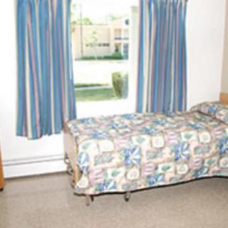 A modest room featuring a single bed with colorful bedding, positioned next to a window with blue striped curtains.