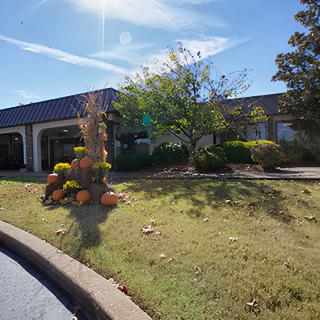 A sunny day view of a building with surrounding trees and flowers.