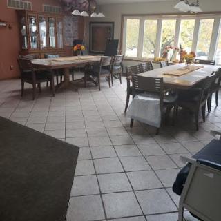 A spacious dining room with large tables and numerous chairs, well-lit by natural light through the windows.