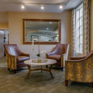 A cozy lobby area featuring elegant armchairs and a round table, with a large mirror on the wall.