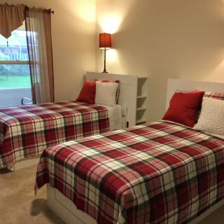 A cozy bedroom with twin beds adorned in red plaid bedding, featuring matching lamps and a window view.