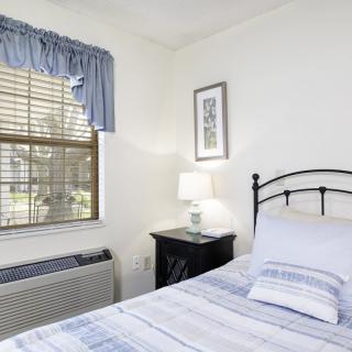 A cozy bedroom with a neatly made bed, a window with blue curtains, and a lamp on the nightstand.