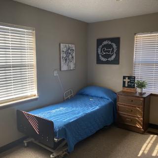 A cozy room featuring a hospital bed with a blue blanket, surrounded by natural light from the windows.