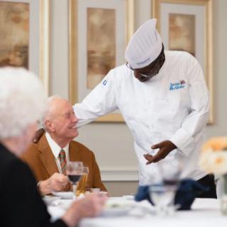 A chef engages with guests in a restaurant setting, showcasing hospitality.
