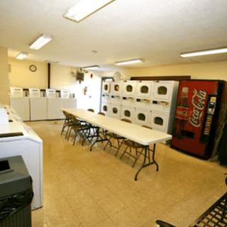 An indoor laundromat with multiple washing machines, dryers, a vending machine, and tables with chairs.