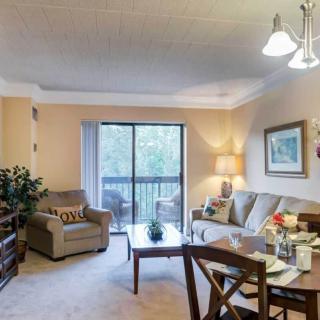 A cozy living room with a sofa, armchair, and dining area, featuring a large window allowing natural light.