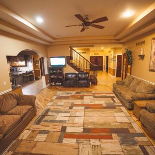 Spacious living room with cozy seating, a colorful rug, and a television near the staircase.