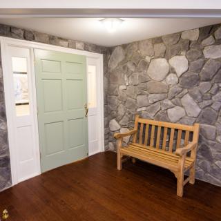 An interior space featuring a stone accent wall, wooden bench, and a light green door.