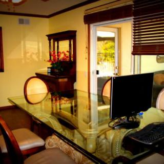 A home office setup with a glass desk, computer, and seating area in a warmly lit room.